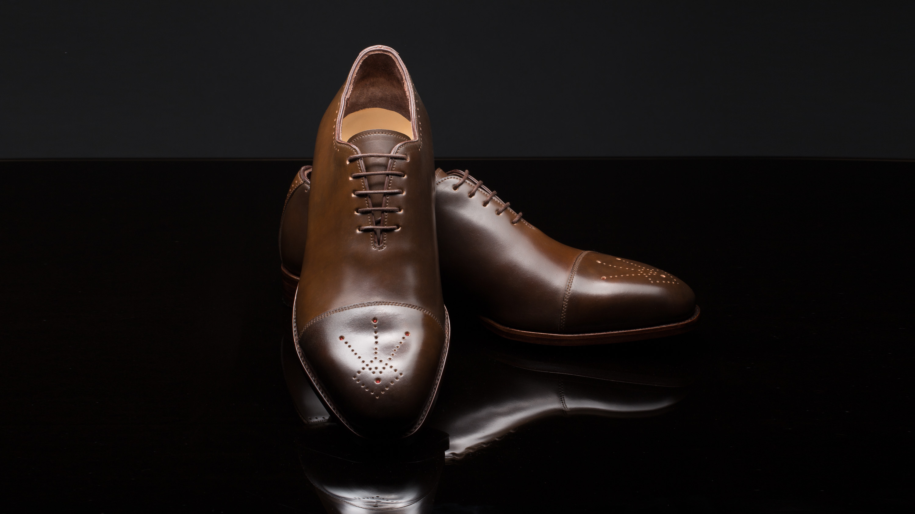 Herren Maßschuhe aus braunem Horween Cordovan mit rot unterlegter Zierlochung Ensemble vor dunklem Hintergrund