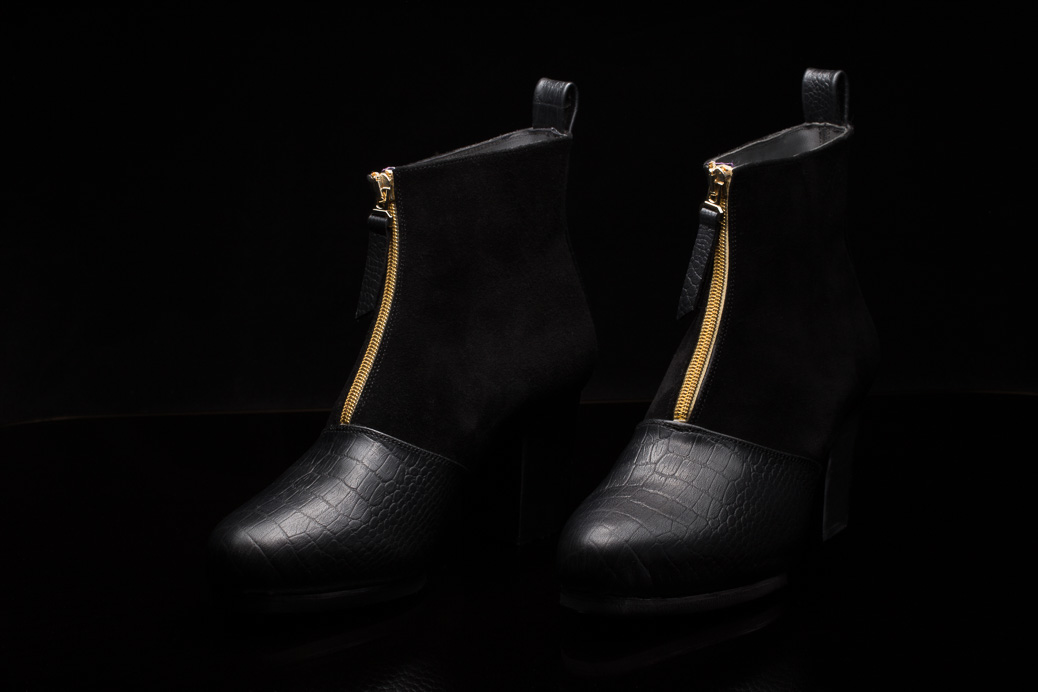 Schwarze Damenstiefeletten mit goldenem Reißverschluss dunkler Hintergrund