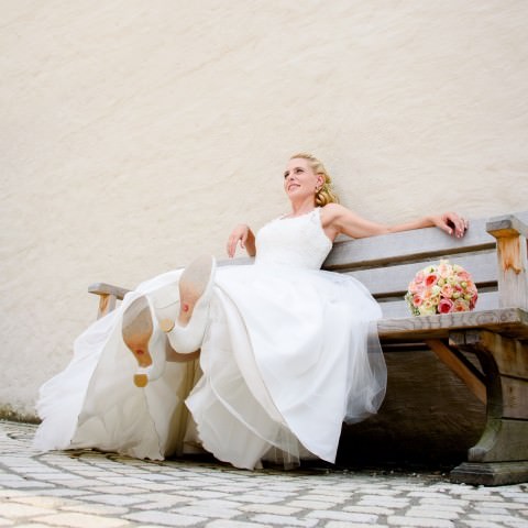 Die Braut sitzt auf einer Bank und trägt ihre Hochzeitsschuhe.